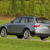 Szary BMW E83 na tle zielonego lasu i łąki.