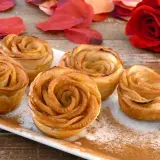 Deliciosas rosas de manzana horneadas, espolvoreadas con canela, junto a pétalos rojos y una rosa natural.