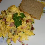 Pyszna jajecznica z boczkiem, pieczarkami i szczypiorkiem, udekorowana natką pietruszki, podana z kromką chleba.