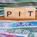 Drewniane klocki z literami "PIT" na tle polskich banknotów. To symbol ulgi na dzieci, która może pomóc w rozliczeniu podatkowym.