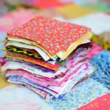 Stos kolorowych kwadratów materiałów, gotowych do stworzenia patchworku. To właśnie patchwork – sztuka łączenia skrawków tkanin w piękne wzory.