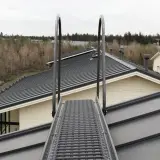 Metalowe stopnie kominiarskie na dachu domu, prowadzące w stronę lasu.