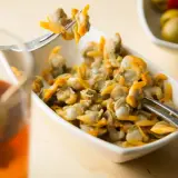 Un plato de berberechos, pequeños moluscos marinos, listos para disfrutar. Se ven deliciosos junto a un vaso de bebida y aceitunas.