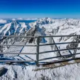 Widok z tarasu widokowego na szczycie Łomnicy. Stalowe balustrady i schody prowadzą do zapierającej dech w piersiach panoramy ośnieżonych gór.