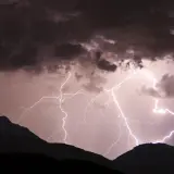Gewitter in den Bergen: Blitze zucken durch dunkle Wolken über silhouettierten Gipfeln.