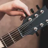 Dłoń kręci kluczem przy główce gitary elektrycznej, pokazując jak nastroić gitarę elektryczną bez stroika, słuchając dźwięku.