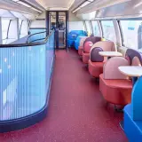 Wnętrze pociągu TGV inOui z kolorowymi siedzeniami i stolikami.