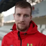 Młody piłkarz w czerwonej bluzie z herbem Korony Kielce, gotowy na nowe transfery.