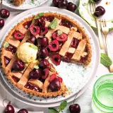 Una deliziosa crostata di ciliegie, guarnita con ciliegie fresche, gelato alla vaniglia e foglioline di menta. Perfetta per un dolce estivo.