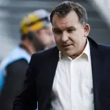 Żyżyński dziennikarz sportowy w garniturze, z uwagą obserwuje wydarzenia na boisku.