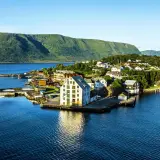 Malowniczy widok na Ålesund Vigra z domkami nad wodą i zielonymi wzgórzami w tle.