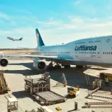 Lufthansa bagaż podręczny czeka na załadunek obok gigantycznego Boeinga 747-400 na lotnisku.