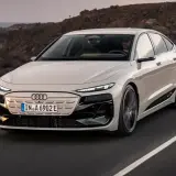 Elegancki Audi A6 e-tron w kolorze kremowym przemierza malowniczą, nadmorską drogę.