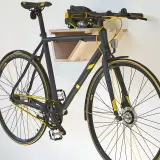 Schwarzes Fahrrad mit gelben Akzenten hängt an einer selbstgebauten Holz-Fahrrad-Wandhalterung. Helm liegt auf der Ablage.