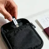 Hand steckt USB-Stick als Festplatte in schwarze Tasche neben Reisepass und Flugticket.