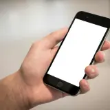 Dłoń trzyma smartfon z pustym ekranem, idealny do pokazania szybkich odpowiedzi SMS, przykładów komunikacji.