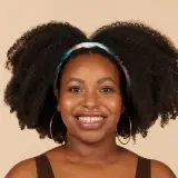 Lächelnde Frau mit voluminösen 4c Locken und einem bunten Haarband.