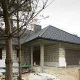 Budowa domu w toku. Widać białe płyty styroduru przy ścianach, które będą izolacją. Obok stoi przyczepa kempingowa.