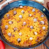 Arroz con caracoles, un plato tradicional español, se presenta en una paellera, adornado con caracoles y trozos de chorizo.