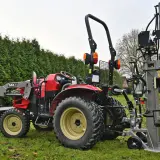 Roter Traktor mit Frontlader und einem liegenden Holzspalter gebraucht 30t im Garten.