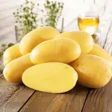 Ein Haufen frischer Kartoffeln, die an ihre Herkunft erinnern, liegen auf einem Holztisch. Daneben ein Glas Öl und Kräuter.