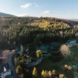 Kolorowy kompleks budynków, w tym hotel i kościółek, otoczony lasem. To idealne miejsce na **centrum rekreacji i sportu**, gdzie można odpocząć wśród natury.
