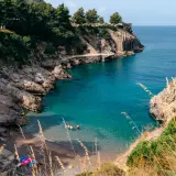 Una piccola spiaggia a Sorrento, con acque cristalline e rocce scoscese. Alcune persone si rinfrescano in mare.