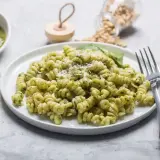 Pyszny makaron z pesto ze słoika, posypany parmezanem. Obok miseczka z zielonym sosem i kawałki sera.