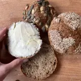 Bułki z serka wiejskiego bez mąki, jedna posypana sezamem, druga pestkami dyni, a jedna połówka z masłem.