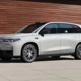 Elegante auto elettrica Leapmotor C10 color argento metallizzato, con un design moderno e linee aerodinamiche, parcheggiata davanti a una parete di legno.