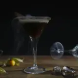 Ein dampfender Espresso Martini mit Zimt und einer kleinen Espressotasse daneben.