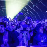 Tłum na fest festiwalu nagrywa koncert telefonami. Światła sceny oświetlają twarze ludzi.