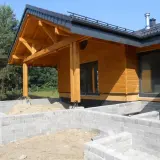 Drewniany dach krokwiowy nad wejściem do domu w budowie, z widocznymi belkami i elementami konstrukcyjnymi.