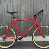 A vintage red Gary Fisher Advance mountain bike with tan tires stands against a wooden fence.