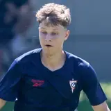 Młody chorwacki piłkarz w granatowej koszulce z logo klubu i Reebok, skupiony na boisku.