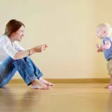 Mamma incoraggia il suo bambino, che sta imparando quando iniziano a camminare i bambini, a fare i suoi primi passi.