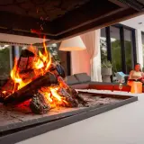 En kvinna läser en bok vid en brasa med elda granved.
