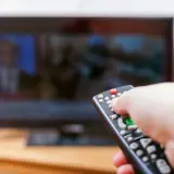 Dłoń z pilotem przed telewizorem, być może to już koniec abonamentu rtv i czas na zmiany.