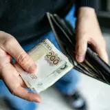 Dłonie trzymające polskie banknoty 200 zł i pusty portfel. Może to symbolizować trudności finansowe lub oczekiwanie na świadczenie pielęgnacyjne.