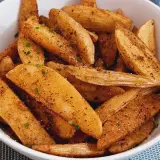 Un tazón lleno de patatas deluxe crujientes, sazonadas con especias y hierbas frescas.