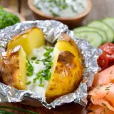 Pommes de terre à la braise, enveloppées dans du papier aluminium, garnies de crème et de ciboulette. Parfait pour le temps de cuisson.