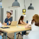 Junge Leute im **Master berufsbegleitend NRW** diskutieren an einem Tisch. Eine Frau schreibt an einer Tafel.