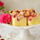 Puszyste ciasto z owocami na oleju, udekorowane różową różą i posypane cukrem pudrem. Idealne na letnie popołudnie.