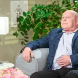 Krzysztof Jackowski w okryciu w kratę, oparty o sofę, jakby snuł najnowsze przepowiednie.