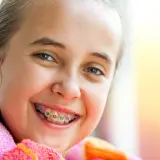 Uśmiechnięta dziewczynka z kolorowym aparatem ortodontycznym, gotowa na wizytę u ortodonty z dzieckiem.