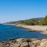 Côte rocheuse et mer bleue près d'une ville côtière en Italie, Imperia, avec des palmiers et des pins.