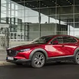 Czerwona Mazda CX-30 lśni przed nowoczesnym budynkiem z przeszkloną fasadą.
