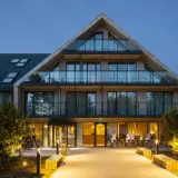 Nowoczesny budynek Saltic Resort & Spa Łeba z betonowymi elementami i przeszklonymi balkonami, oświetlony wieczorem.