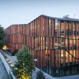 Nowoczesna architektura Małopolskiego Ogrodu Sztuki w Krakowie, z drewnianą fasadą i przeszklonymi wnętrzami, tworzy rajską oazę dla kultury.