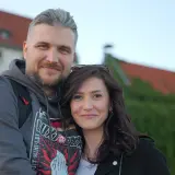 Ewa Zajączkowska-Hernik i jej mąż, uśmiechnięci na tle zabytkowych budynków.